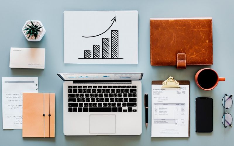 feature image of Blog 7 Ways To Promote Your Retail Brand Online displaying a table full of stationery with a coffee cup and a laptop placed in an organized manner