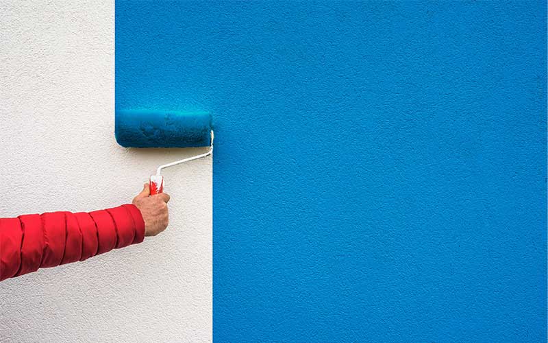 Man painting a white wall i sky blue paint with a roller