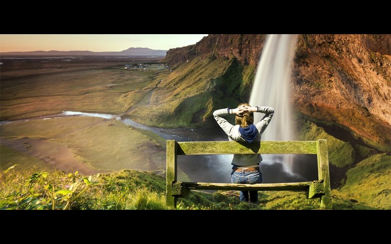A scenery with waterfall and a girl sitting on bench