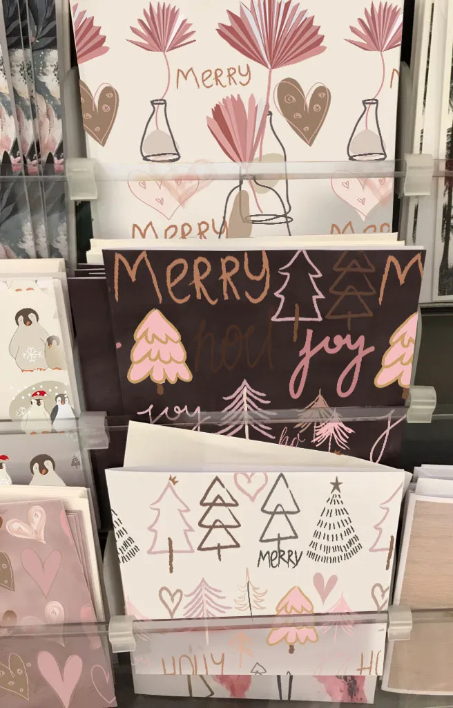 A rack of Christmas cards displays hand-drawn trees, hearts, and holiday words.