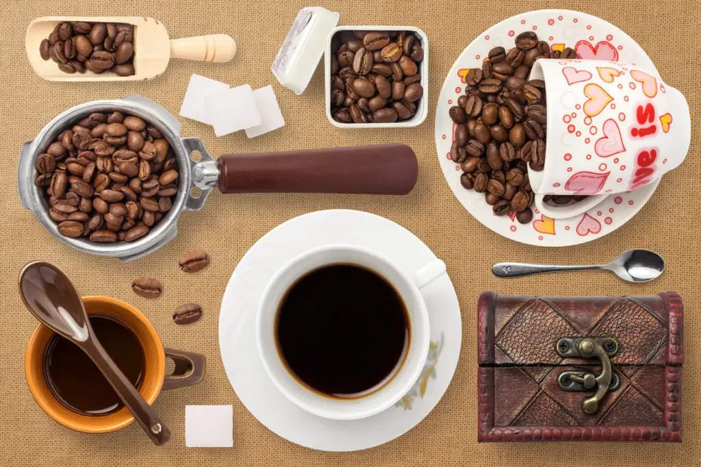 A white cup of black coffee surrounded by beans, scoops, cups, and a decorative chest on a burlap surface