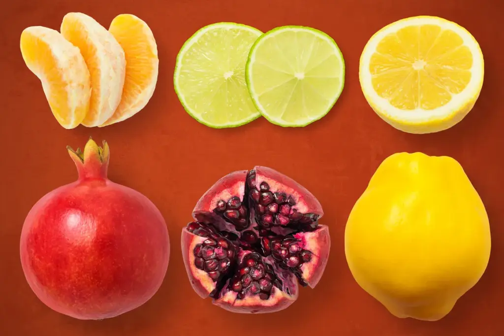 Peeled orange, lime slices, lemon half, whole and halved pomegranate, and quince arranged on a reddish-brown background