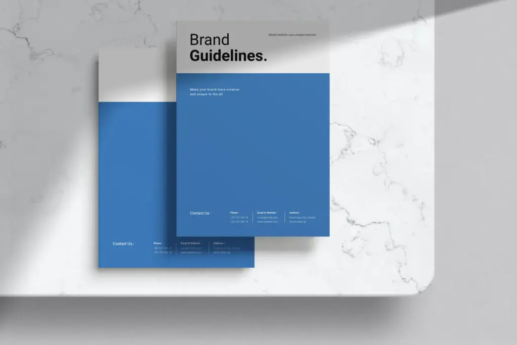 Two vertical brand guideline covers on a marble surface, showing the blue and white design with contact information.