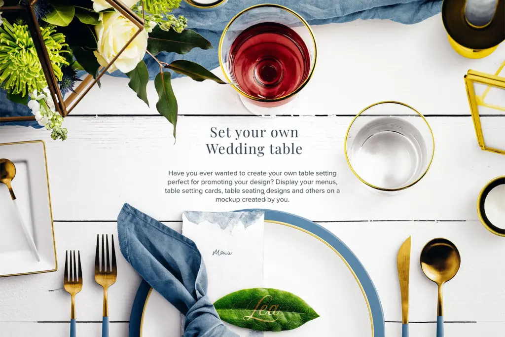 Wedding table setting mockup with a plate, gold utensils, wine glass, napkin, and floral arrangement on a white wood surface.