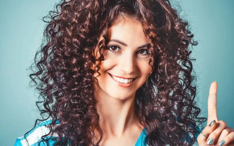 Woman with curly hair cleanly extracted and placed on a solid teal background after using AI edge detection in CutOut 11.